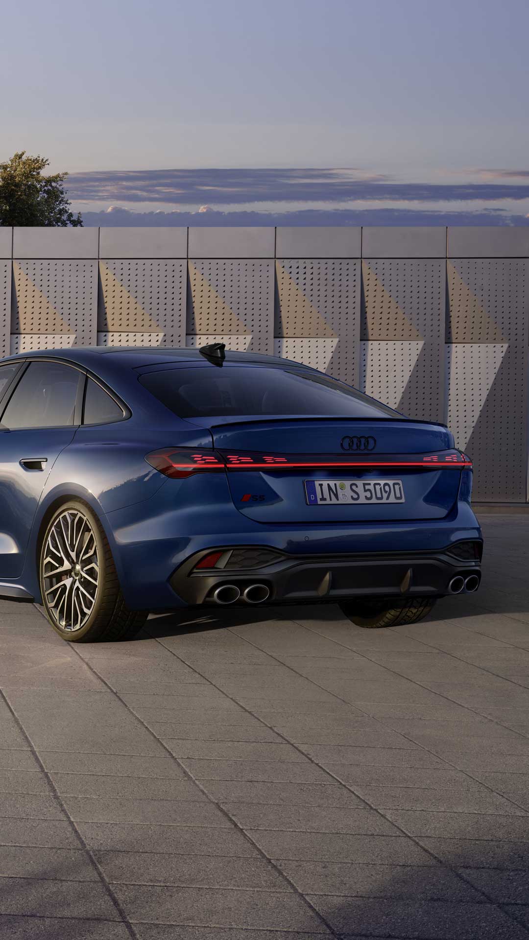 Die S5 Limousine in dunkelblau steht schräg vor einer Gebäudefassade und wird dabei vom Sonnenlicht angestrahlt.