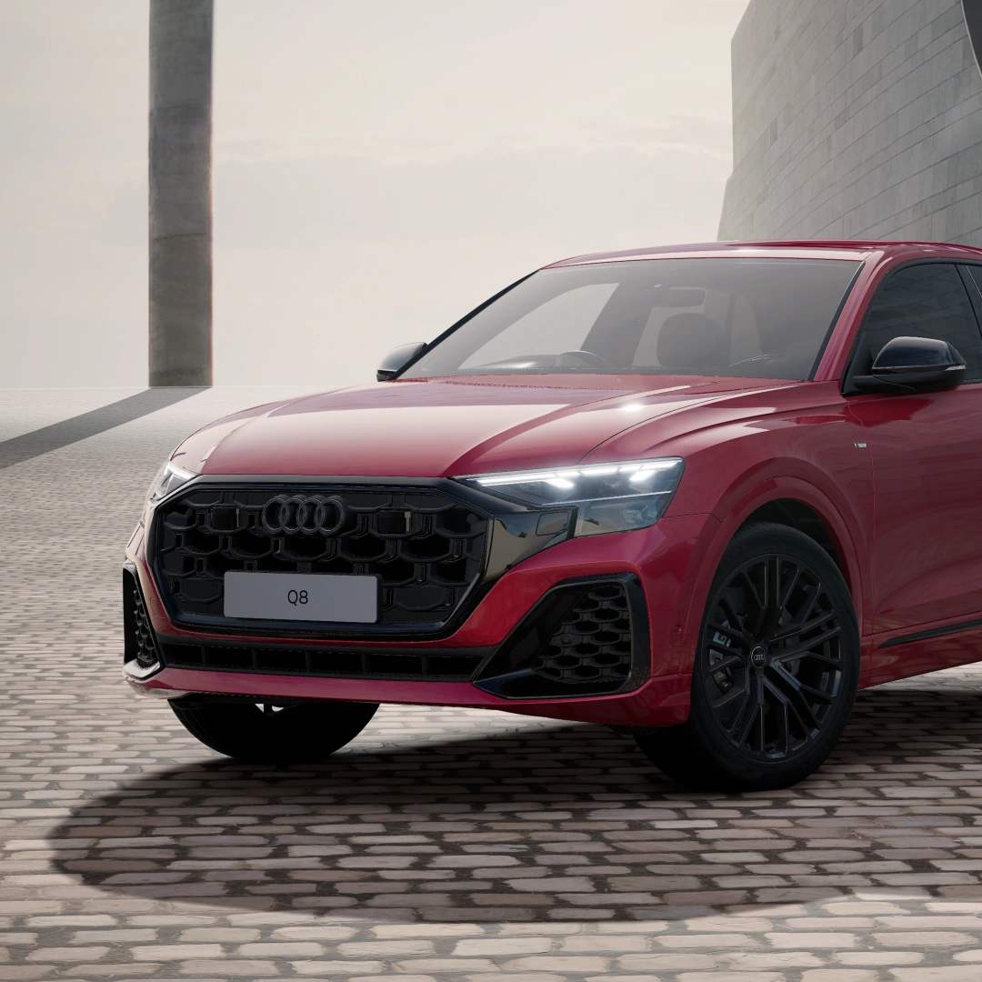 Front three-quarter view of a red Audi Q8 e-hybrid SUV in Black Edition trim, parked on cobbled paving, with a black Singleframe grille and black alloy wheels.