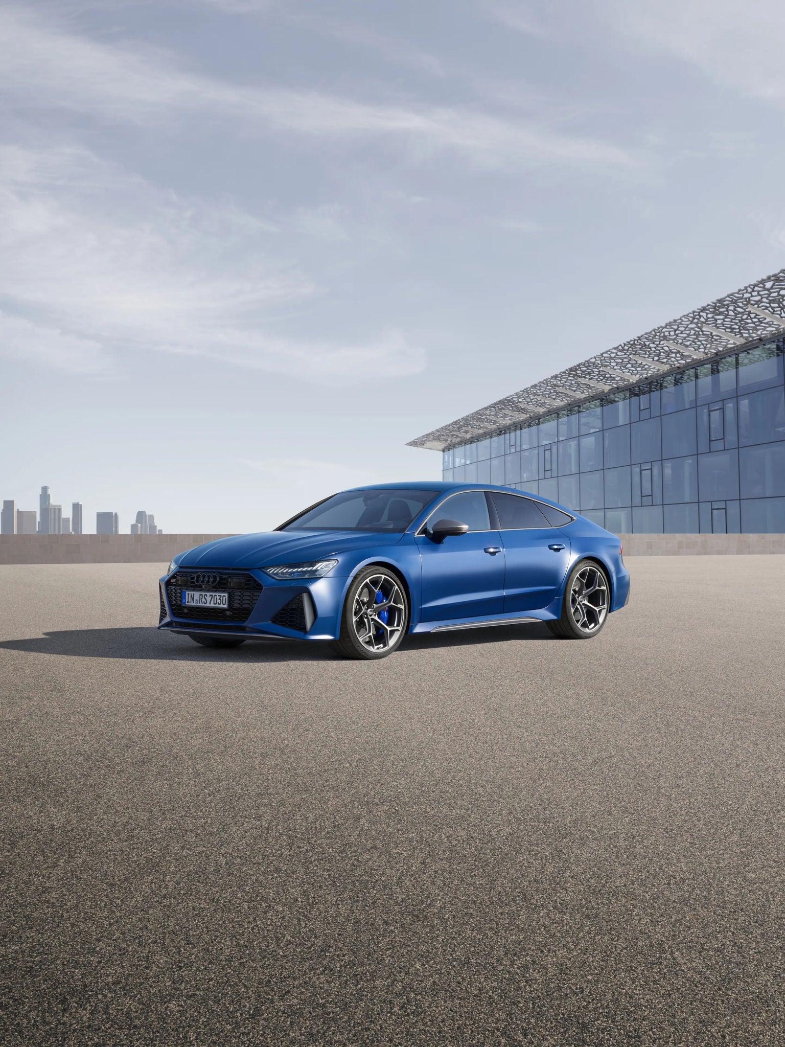 Blue sedan parked outside a modern building with a distant city skyline in the background.