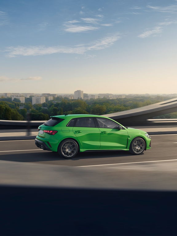 Grüner Audi RS 3 Sportback fährt auf mehrspuriger Straße, Seitenansicht mit Fokus auf Felgen und Fahrzeugkontur.