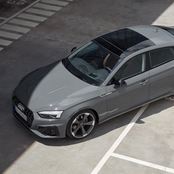 Aerial view of a grey Audi parked diagonally across the lines in a parking lot.