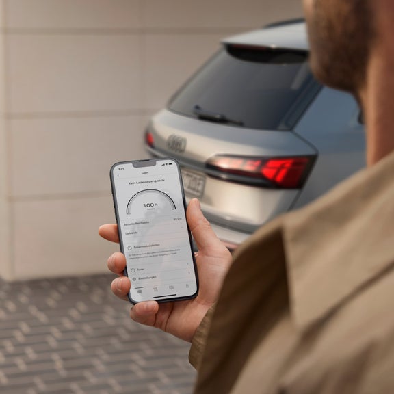 Person checks car charge status on a smartphone app, with vehicle in background.