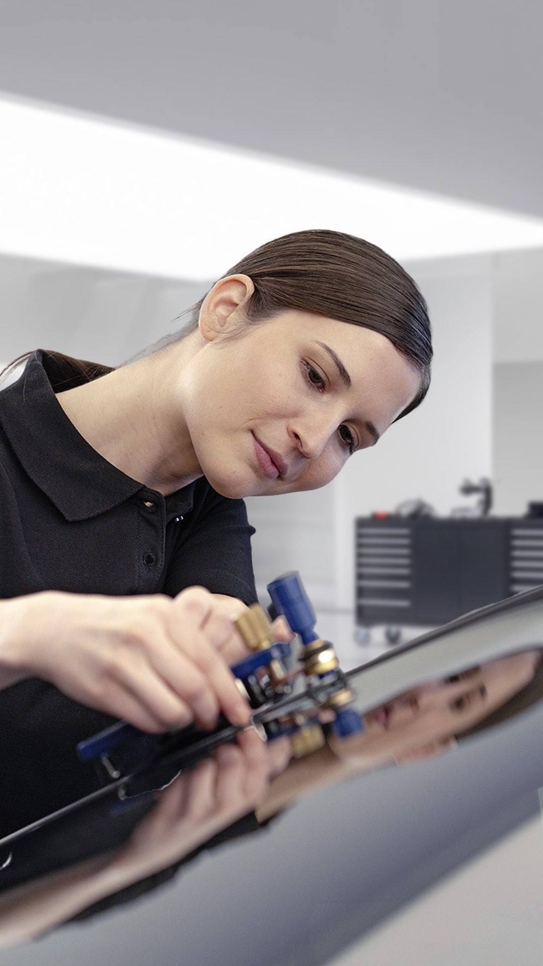 Audi-Mitarbeiterin repariert mit einem Spezialwerkzeug einen Steinschlag an der Windschutzscheibe eines Fahrzeugs.
