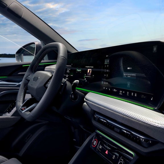 Interior view of Audi dashboard, featuring a sleek design with digital displays and green accents, against a scenic backdrop.