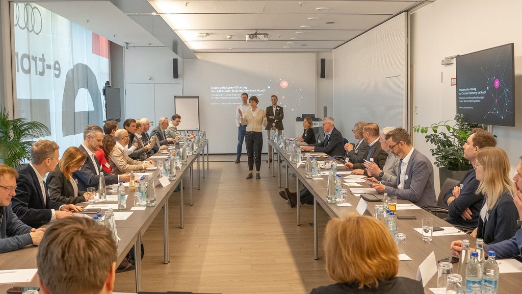 Many people sit at a U-shaped table during a lecture