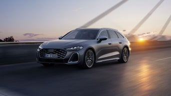 Silver Audi S5 Avant driving over a bridge at sunset, with sleek design and sharp headlights. The setting sun casts a warm glow on the road. Sporty and dynamic.
