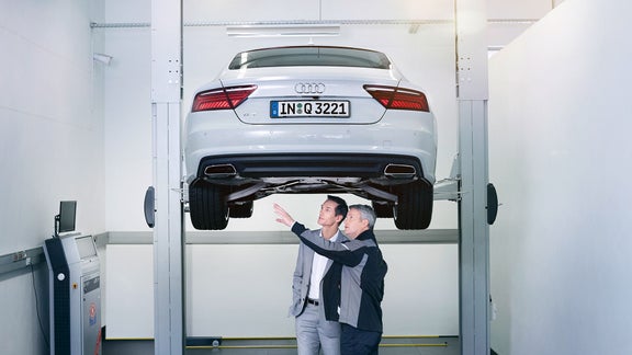 En man och en av Audis servicepersonal står bredvid varandra under en Audi Q3 som är upphöjd på en ställning ch tittar mot bilens vänstra bakdäck