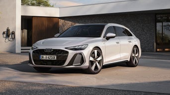 White Audi A6 Avant e-tron parked at a modern home, connected to a charging station.