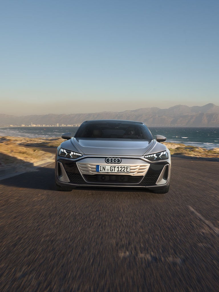 Die Frontansicht des Audi S e-tron GT auf einer kurvigen Küstenstraße. Die markanten LED-Scheinwerfer und das geschlossene, aerodynamische Kühlergrill-Design sind erkennbar.