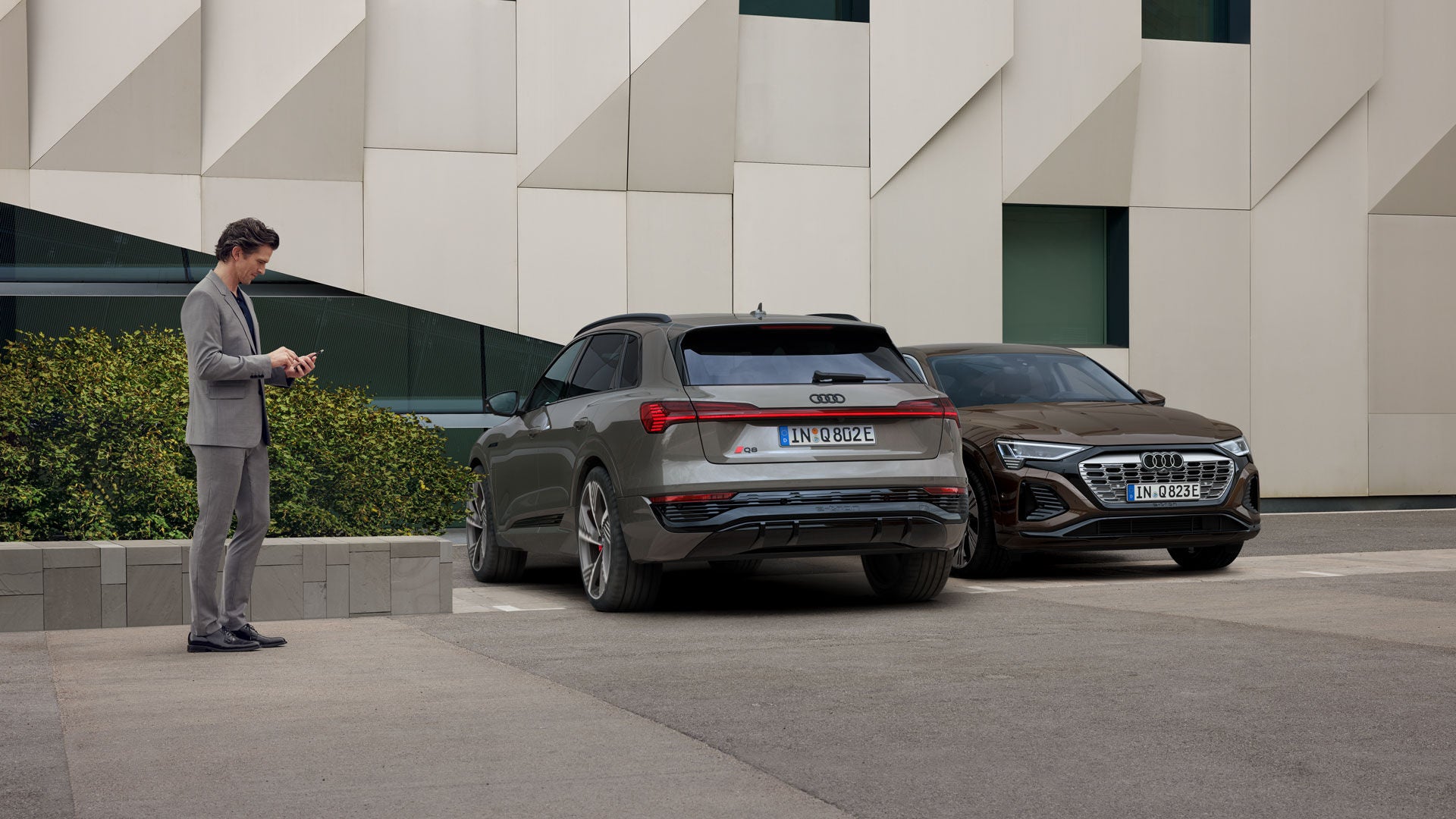 Två Audi står parkerade mot en vägg. En person står bredvid.