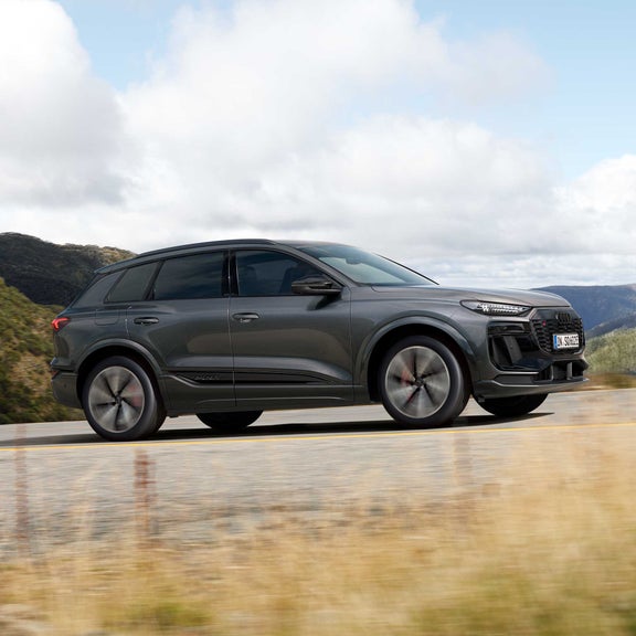 Seitliche Aufnahme des SQ6 SUV e-tron, welcher über eine Straße in einer bergigen Region fährt.