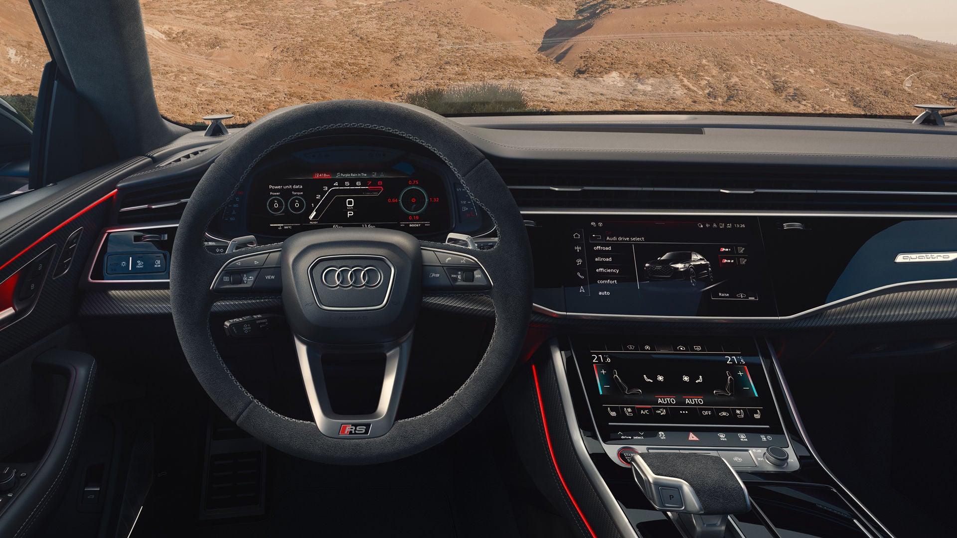 Rear view of the cockpit of the RS Q8 SUV, with a focus on the steering wheel and the digital displays. Through the windshield, barren rocks can be seen.
