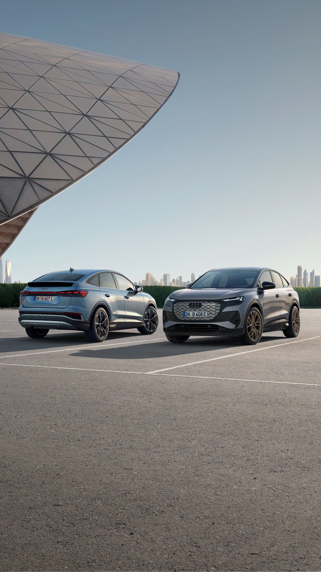 Two electric SUVs parked side by side with a city skyline in the background.