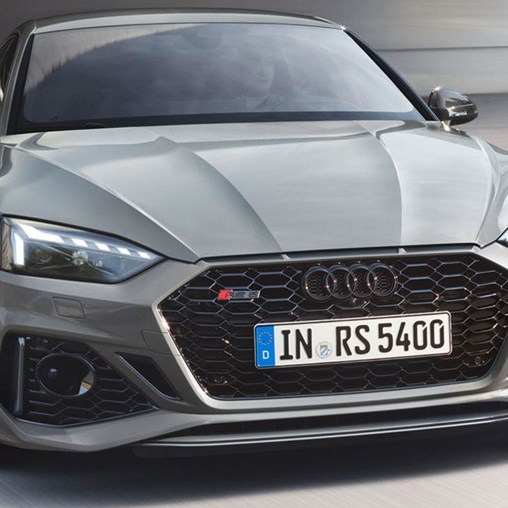 Front view of a moving grey Audi RS 5 Sportback with a visible driver.