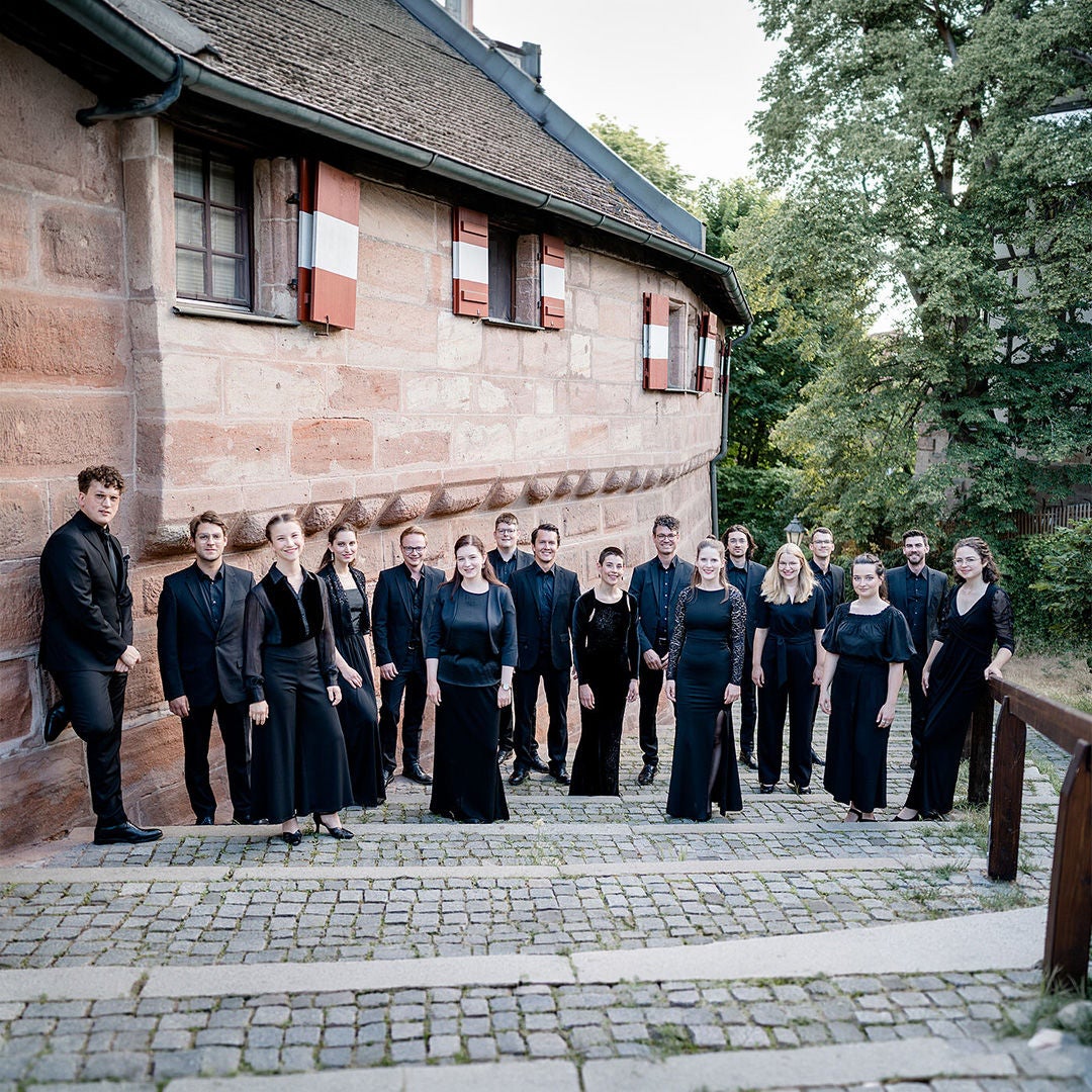 Gruppe von 16 Personen in schwarzer Kleidung vor einem historischen Sandsteingebäude auf Kopfsteinpflaster.