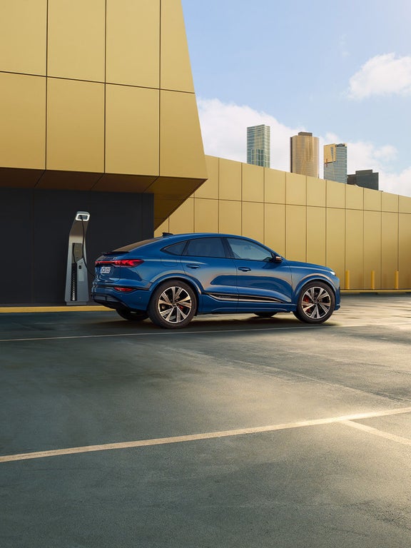 Blauer Audi SQ6 Sportback e-tron von schräg hinten, steht an Ladesäule vor schwarzer und gelber Wand.