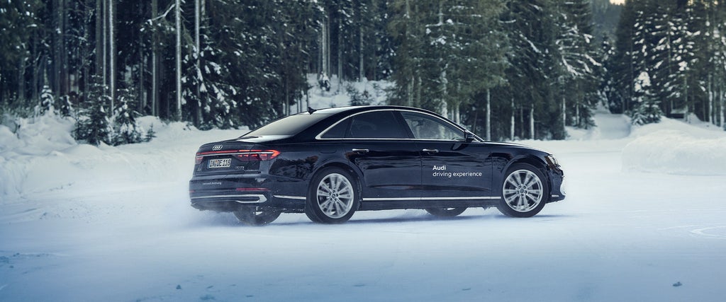 Schwarzer Audi Audi A8 50 TDI quattro fährt im Schnee, im Hintergrund sind Wälder.