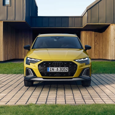 Frontansicht eines gelben Audi A3 allstreet vor einem modernen Holzgebäude mit Rasenfläche.