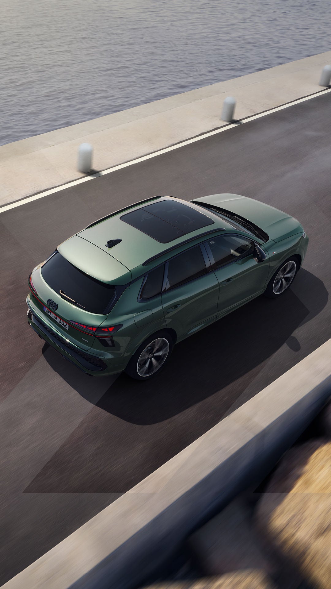 Grüner Audi SUV fährt auf einer Straße am Wasser entlang.