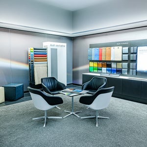Loungebereich im Showroom mit zwei schwarzen Sesseln, Glastisch und Wanddisplay mit Farb- und Materialmustern.