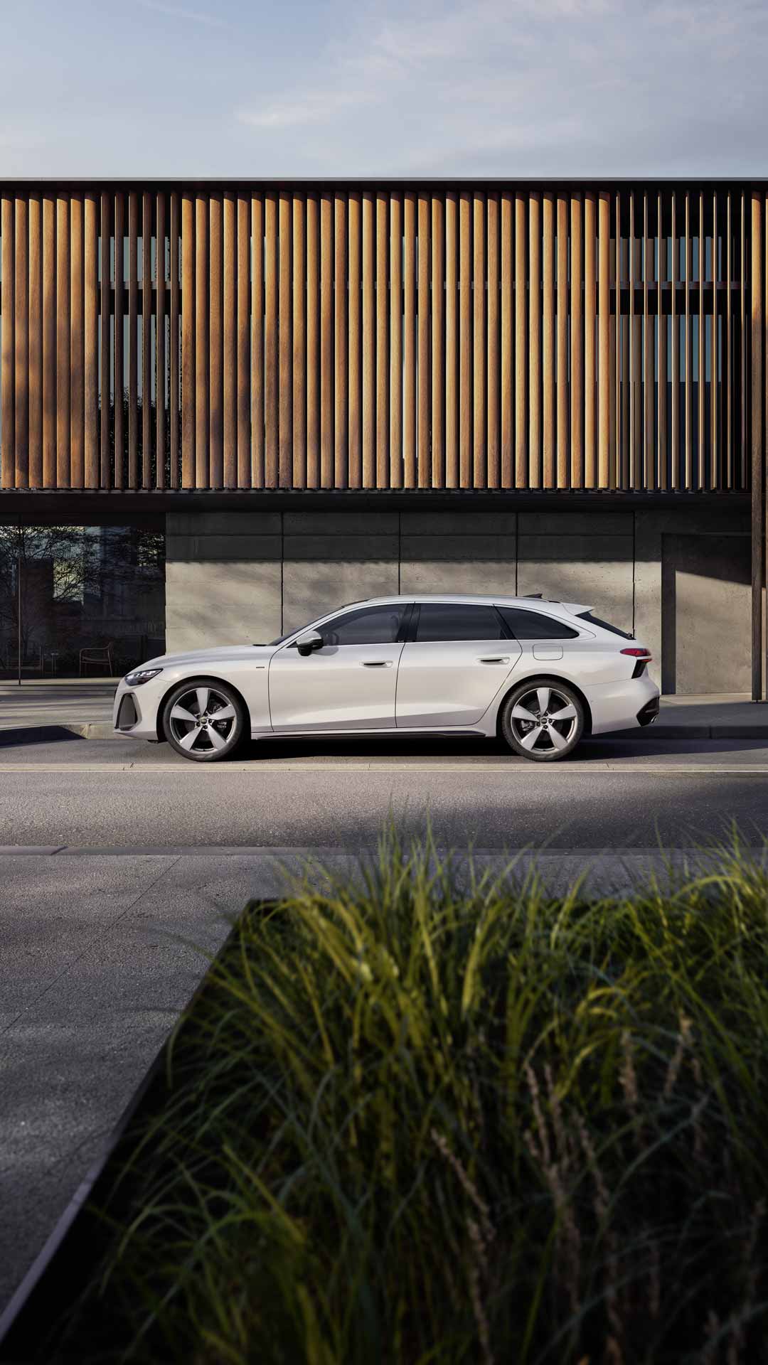 Der A6 Avant e-hybrid steht im Seitenprofil in einer Parkbucht vor der Fassade eines Gebäudes.