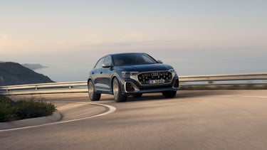 Der SQ8 SUV schräg von vorne passiert eine Kurve auf einer Bergstraße. Im Hintergrund das Meer.