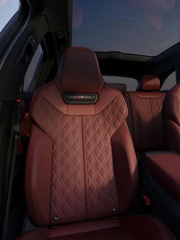 Zwei vordere Sportsitze im Audi S5 Avant in rotem Leder mit gestepptem Muster und „S“-Logo, Panorama-Dach im Hintergrund.