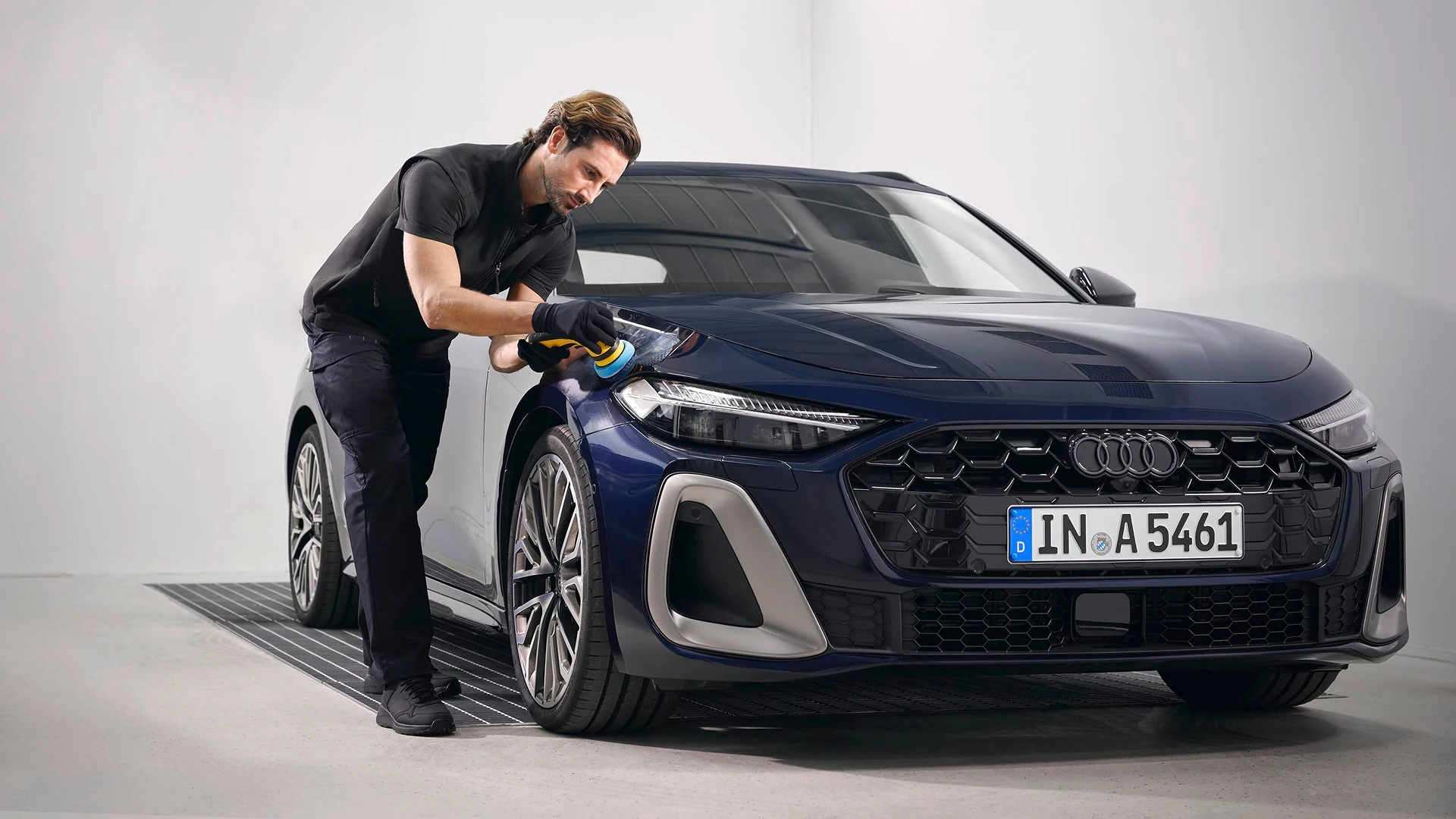 Technician polishing the front headlight and bodywork of an Audi vehicle in a workshop environment.