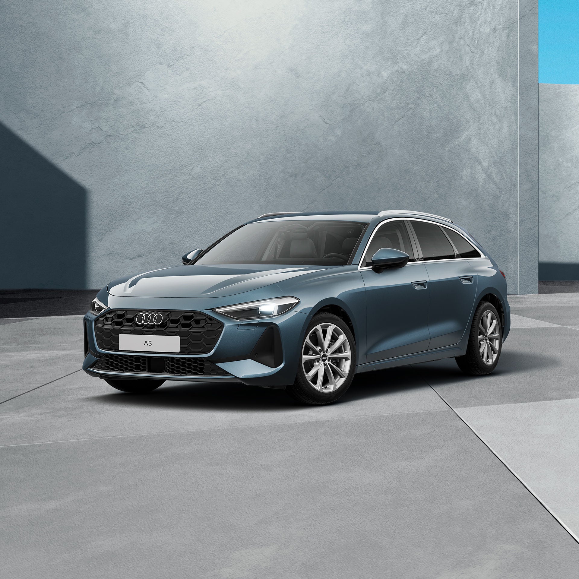 Ein grauer, moderner Avant steht in einem grauen Studio. Das Fahrzeug ist schräg von vorne dargestellt und von natürlichem Licht umgeben.