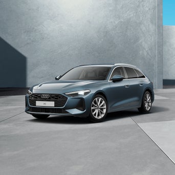 Ein grauer, moderner Avant steht in einem hellen Studio. Das Fahrzeug ist schräg von vorne dargestellt und von natürlichem Licht umgeben.