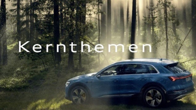 Blauer Audi e-tron steht im Sonnenlicht am Waldrand, darüber der weiße Schriftzug „Kernthemen“ vor bewaldetem Hintergrund.