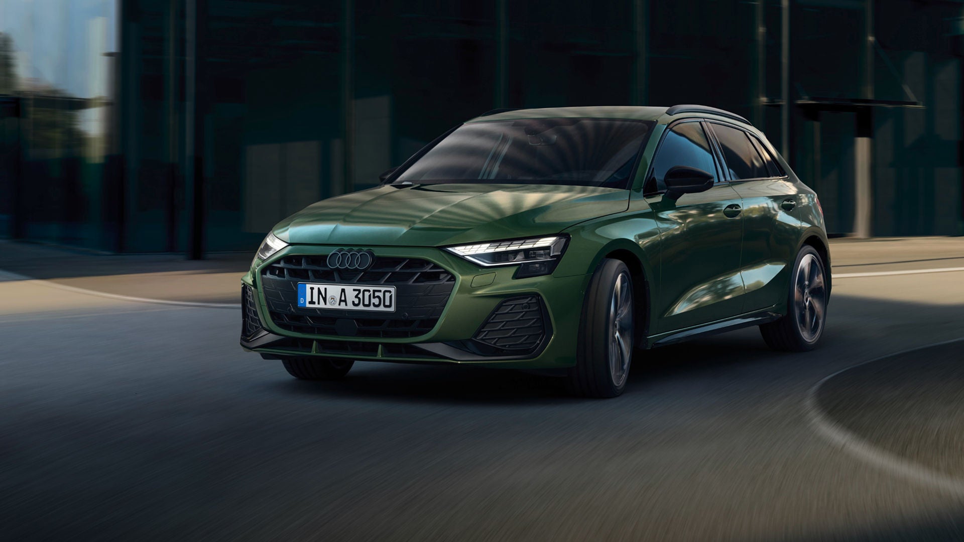 A person standing next to a blue sedan by a waterfront at dusk.