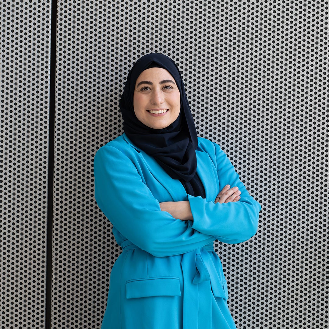 Betül steht mit verschränkten Armen lächelnd vor einer Wand