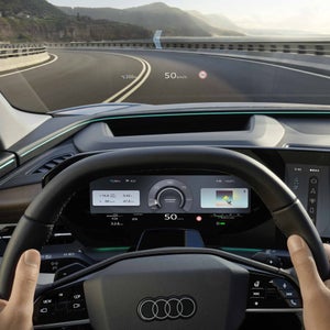 Der Q6 SUV e-tron aus Fahrerperspektive während der Fahrt. Das Head-up-Display zeigt Geschwindigkeit, Geschwindigkeitsbegrenzung, sowie die Navigation und den Verlauf der nächsten Kurve an.