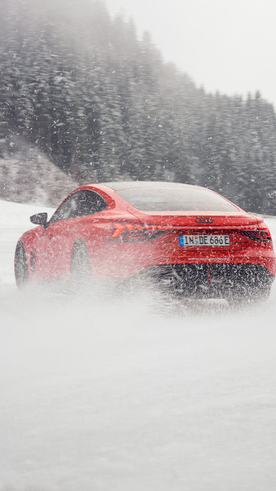 A red Audi RS e-tron GT performance is driving along a snow-covered track; snow kicked up by the tyres is partially obscuring the rear of the car.