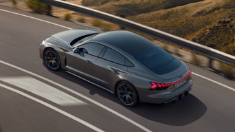 Ein grauer Audi RS e-tron GT fährt auf einer kurvigen Bergstraße mit leuchtenden Rücklichtern.