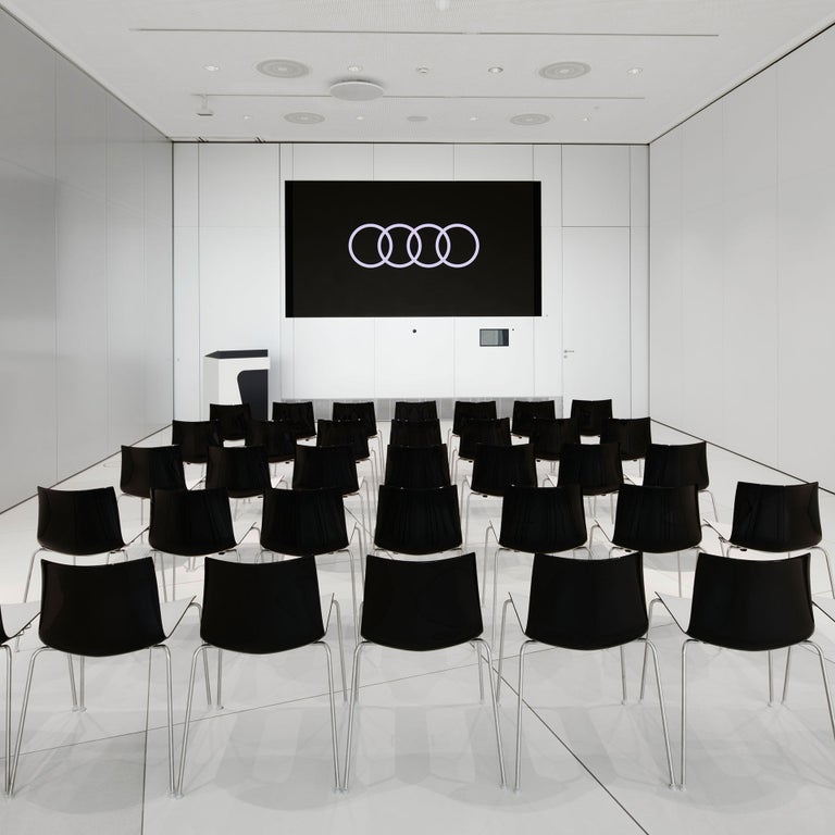 Kleiner, weißer Vortragssaal mit schwarzer Bestuhlung und Audi Logo auf großem Bildschirm.