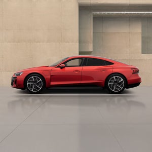 A red electric sedan is showcased against a minimalist concrete background, highlighting its modern design and sporty features.