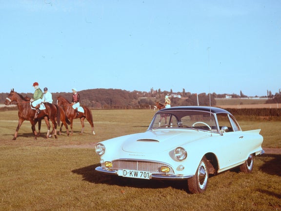 Ein hellblauer Auto Union 1000 SP Coupé steht neben reitenden Personen auf einer Wiese