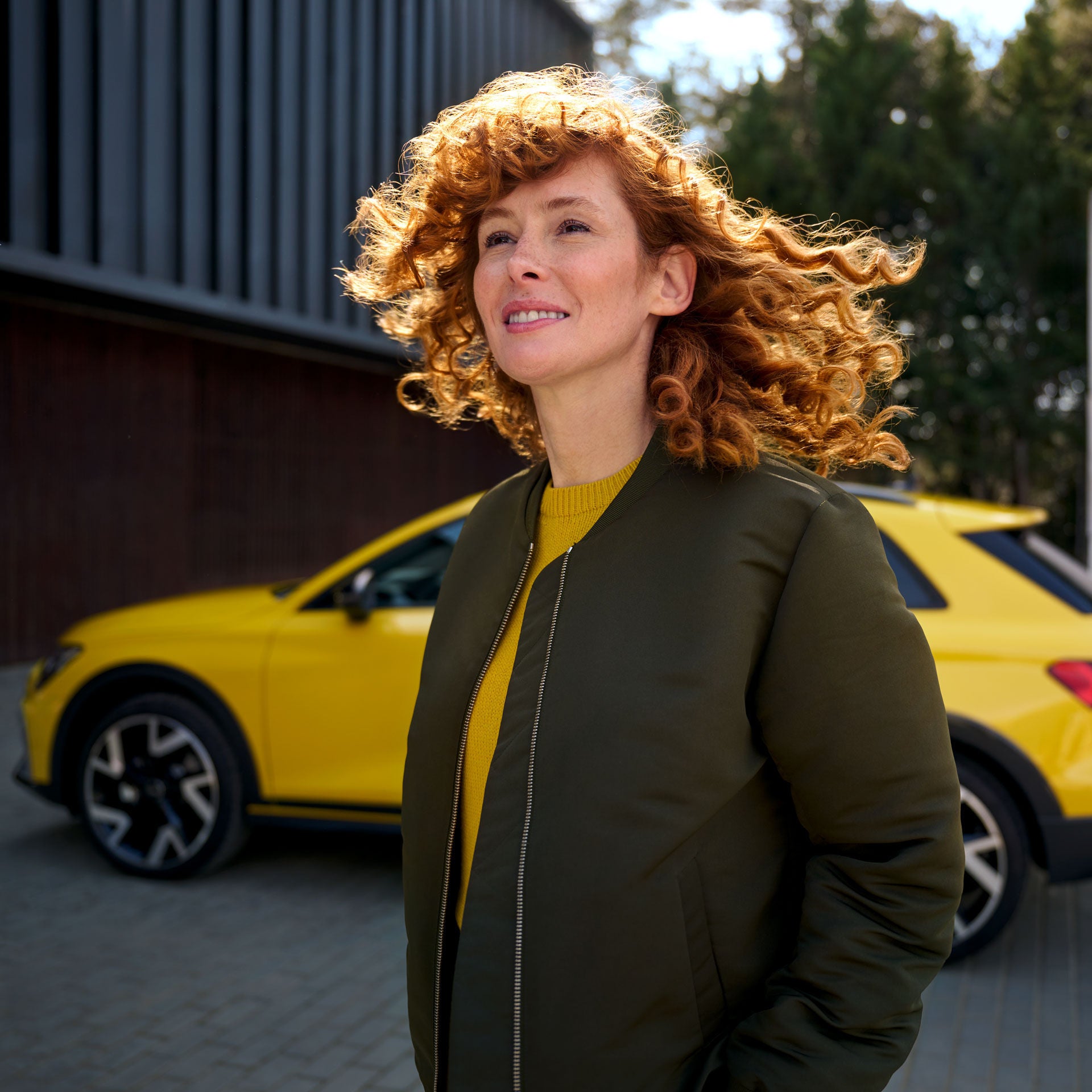 Frau mit roten Locken vor einem gelben Auto