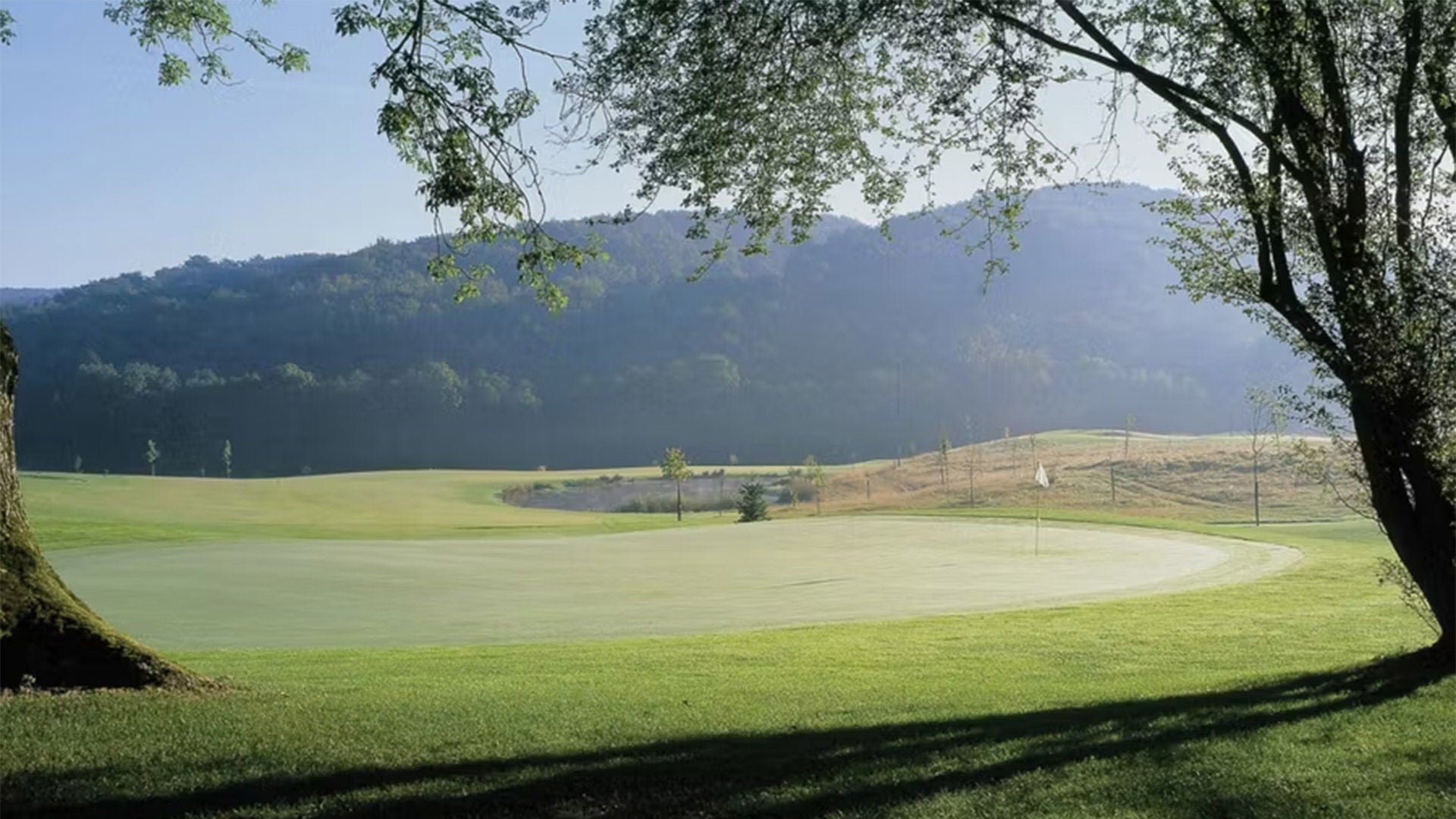 Un terrain de golf verdoyant bordé d'arbres, avec des collines en arrière-plan.