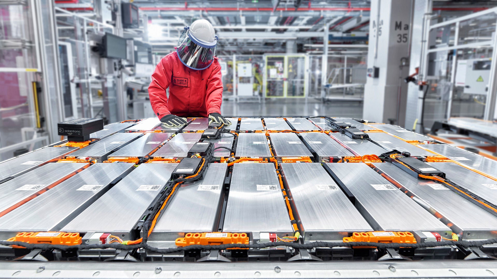 A person in protective clothing working in a production hall on a large battery module.