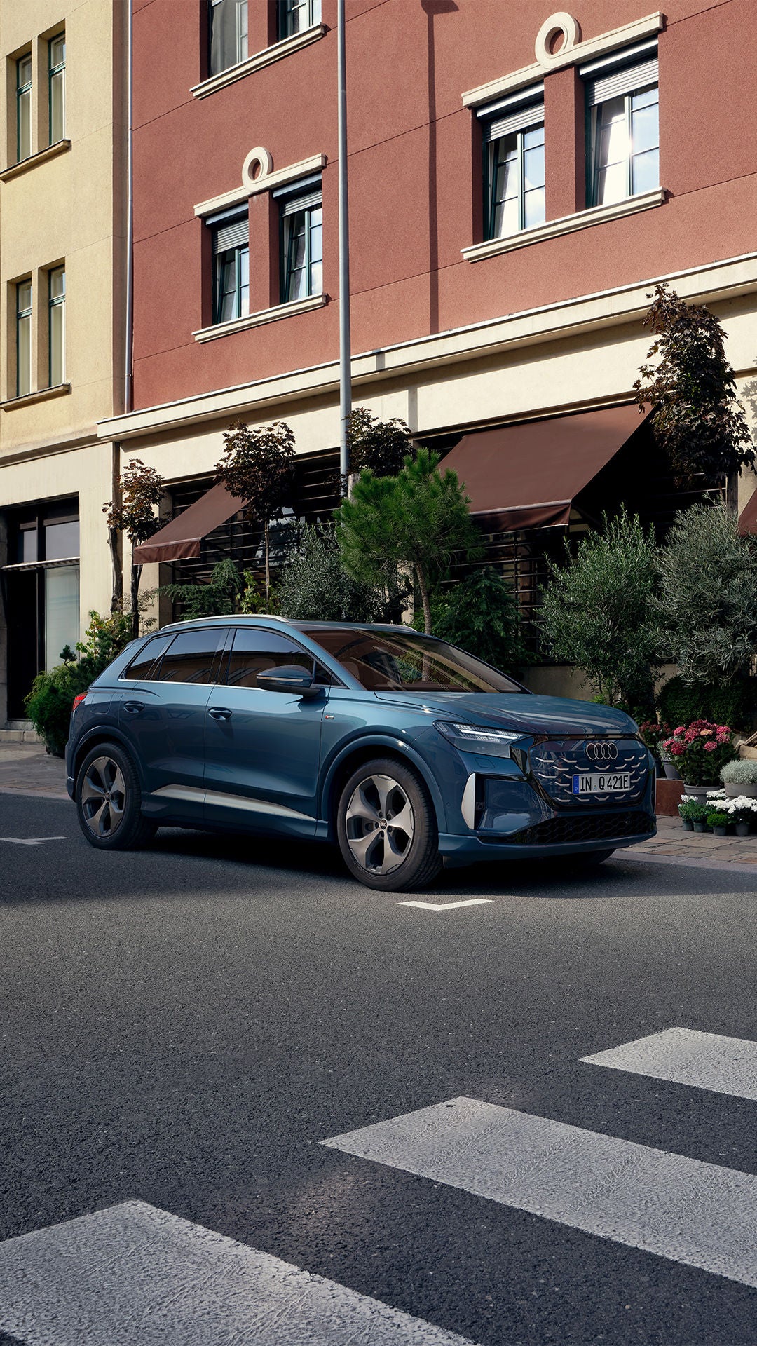 Une Audi Q4 e-tron bleue garée dans une rue bordée de magasins dotés de terrasses et de plantes.