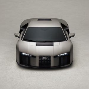 Frontansicht des Audi Nuvolari mit eingeschalteten Scheinwerfern in beige neutralem Studioambiente.