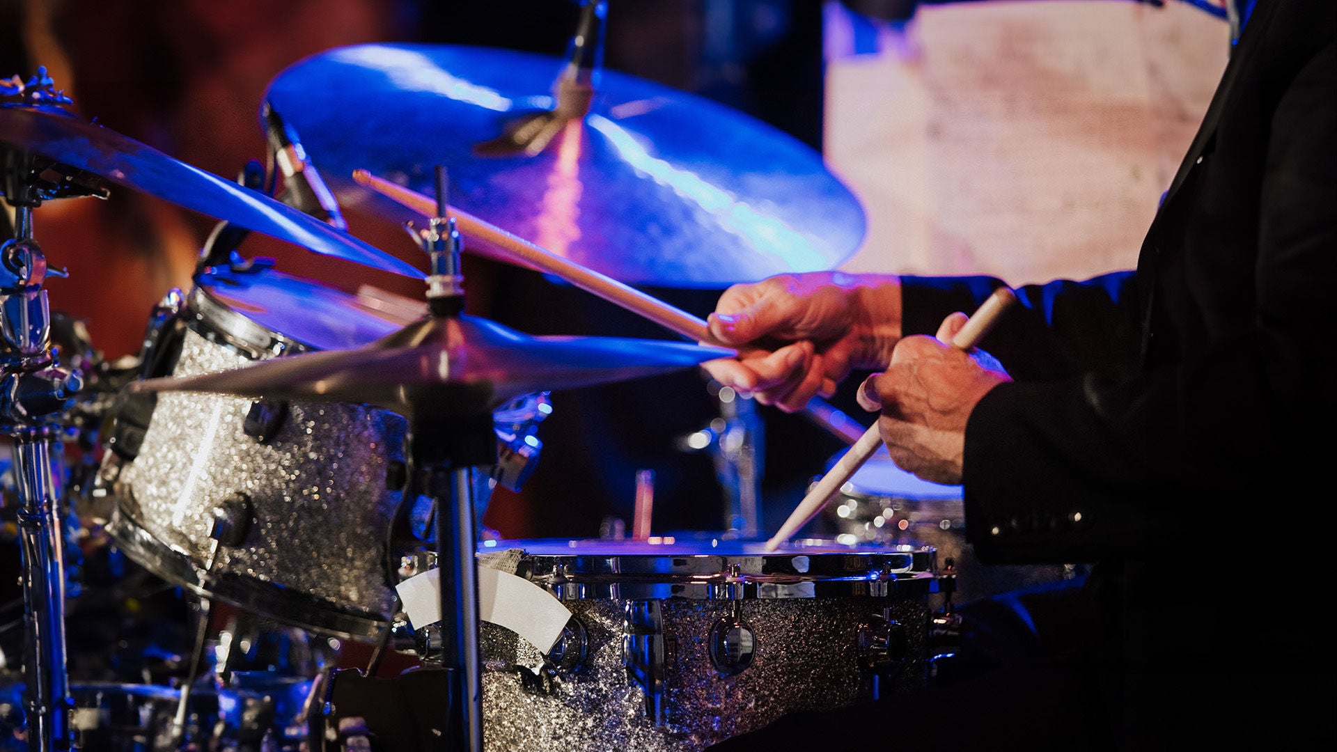 Close-up of a drum set, a person plays with drumsticks on the drums and cymbals.