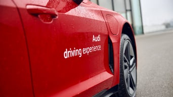 Rotes Audi Modell mit Aufschrift „Audi driving experience“, Nahaufnahme der Seitenpartie mit nasser Karosserie und Vorderrad.