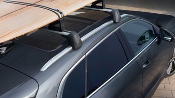 Ein Surfbrett ist mit Halterungen auf dem Dach eines grauen Fahrzeugs befestigt.