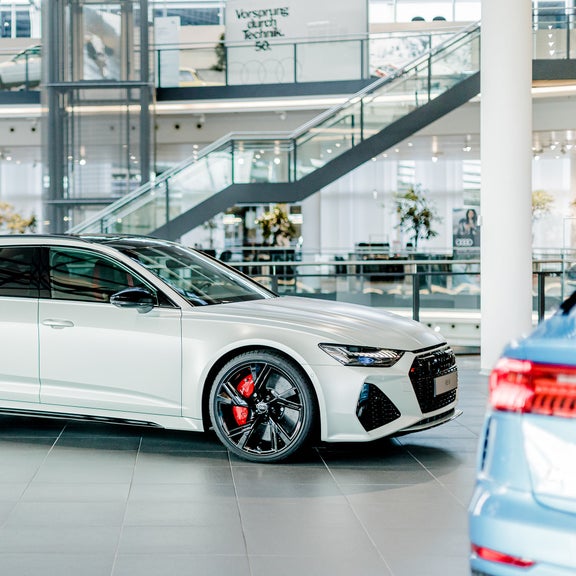 Side view of a white Audi RS 6 Avant with red brake calipers in a modern showroom.