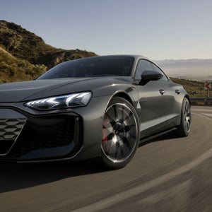 Ein grauer Audi RS e-tron GT fährt auf einer kurvigen Bergstraße bei Sonnenlicht, mit leuchtenden LED-Scheinwerfern.