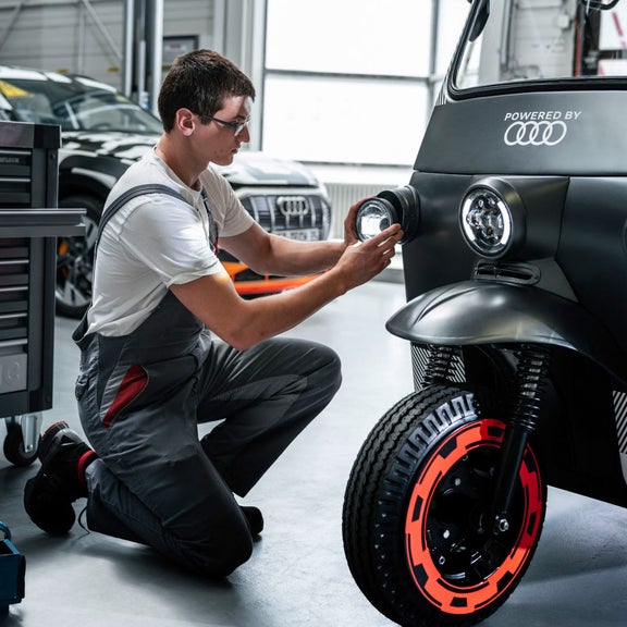 People are standing in a circle. A man squats in front of them and shows them things.